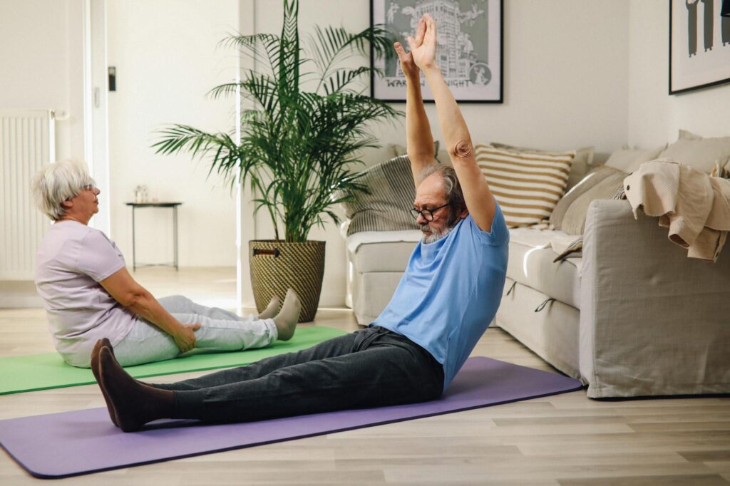Elderly couple enjoying yoga exercise on mats at home, promoting healthy and positive aging.