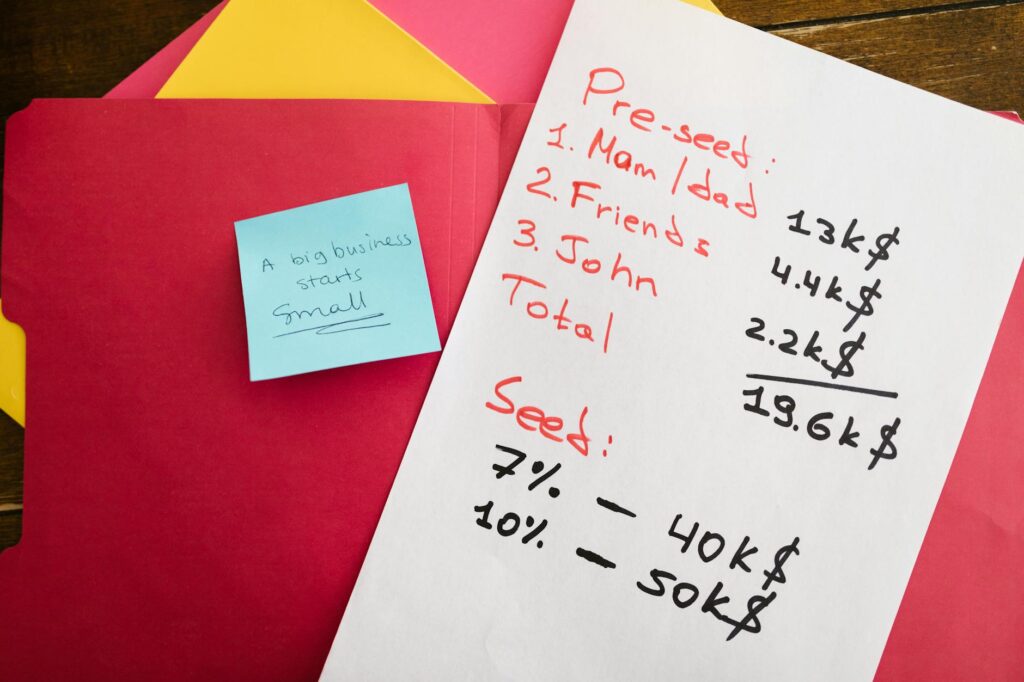 Handwritten notes detailing pre-seed and seed funding with motivational post-it on a desk.