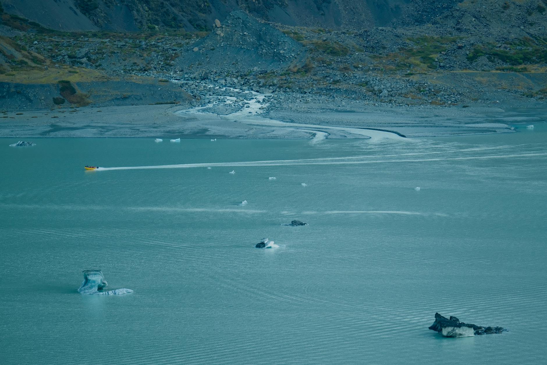 Aerial shot of icebergs floating in Mount Cook lake with a distant yellow boat, New Zealand.