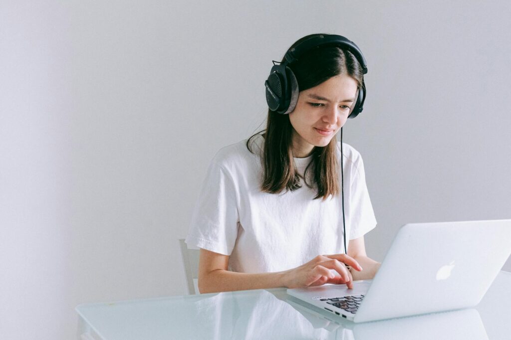 Young woman using laptop with headphones, working remotely in a home office.