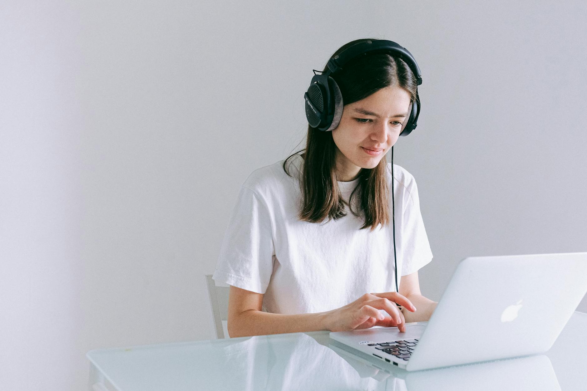 Young woman using laptop with headphones, working remotely in a home office.
