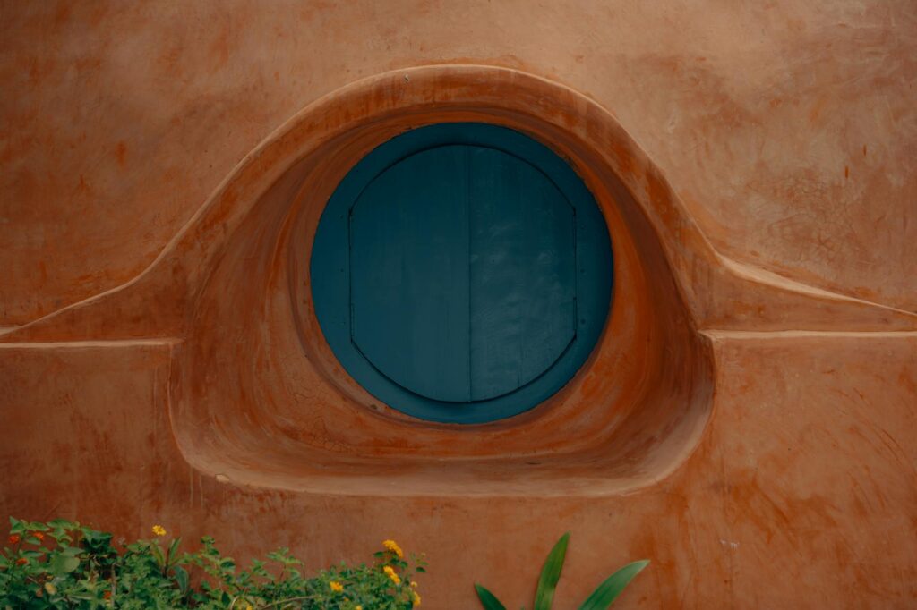 Close-up of a round blue window set in a rustic terracotta wall in Hyderabad, India.