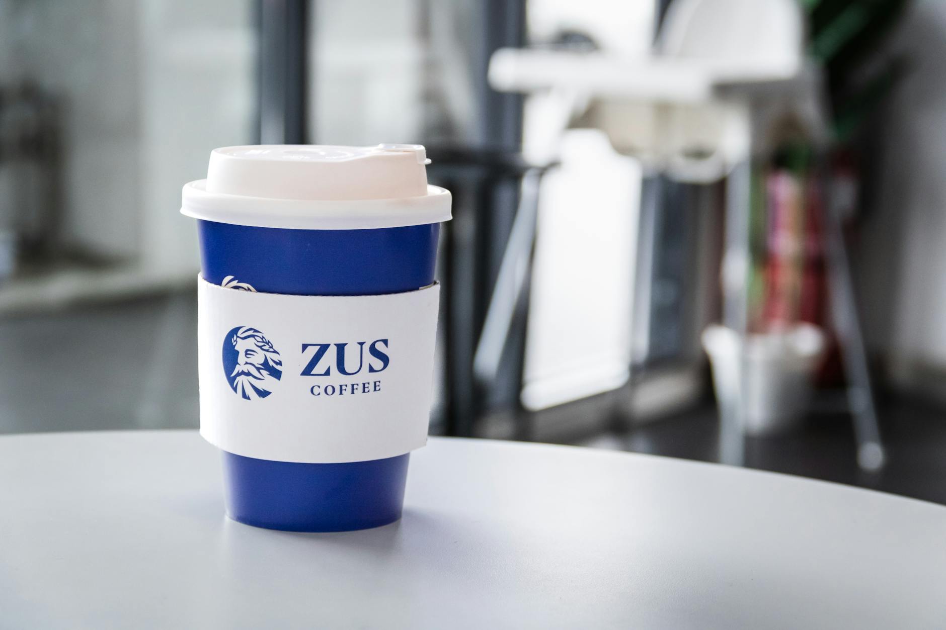 A blue to-go coffee cup from ZUS Coffee on a modern indoor table.