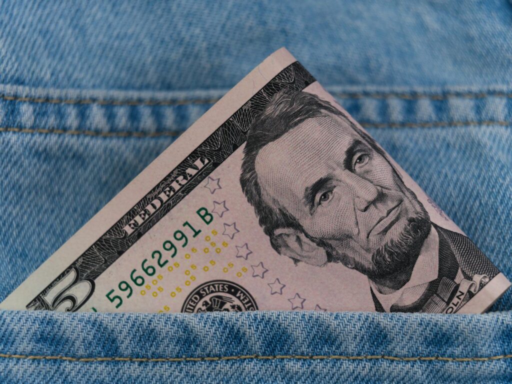 A five dollar bill tucked into a blue denim jeans pocket, symbolizing savings or cash on the go.