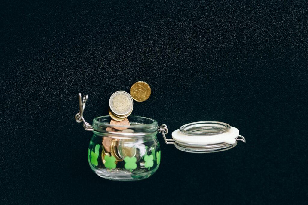 Glass jar with coins falling into it on a black background, symbolizing savings.