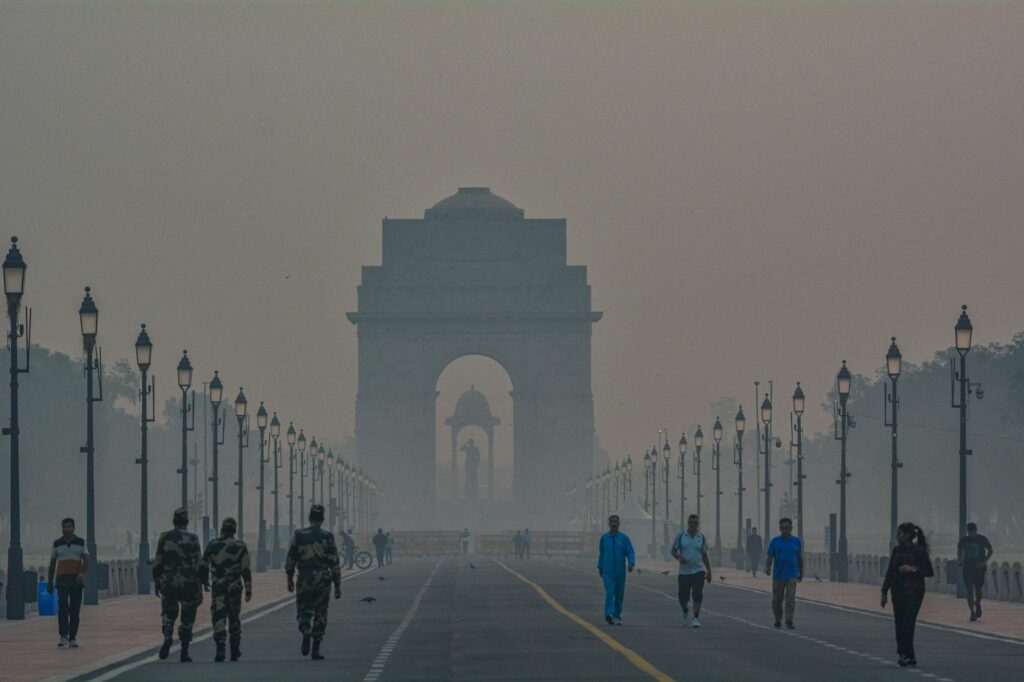 A foggy morning scene with pedestrians near India Gate in New Delhi, highlighting the landmark's grandeur.