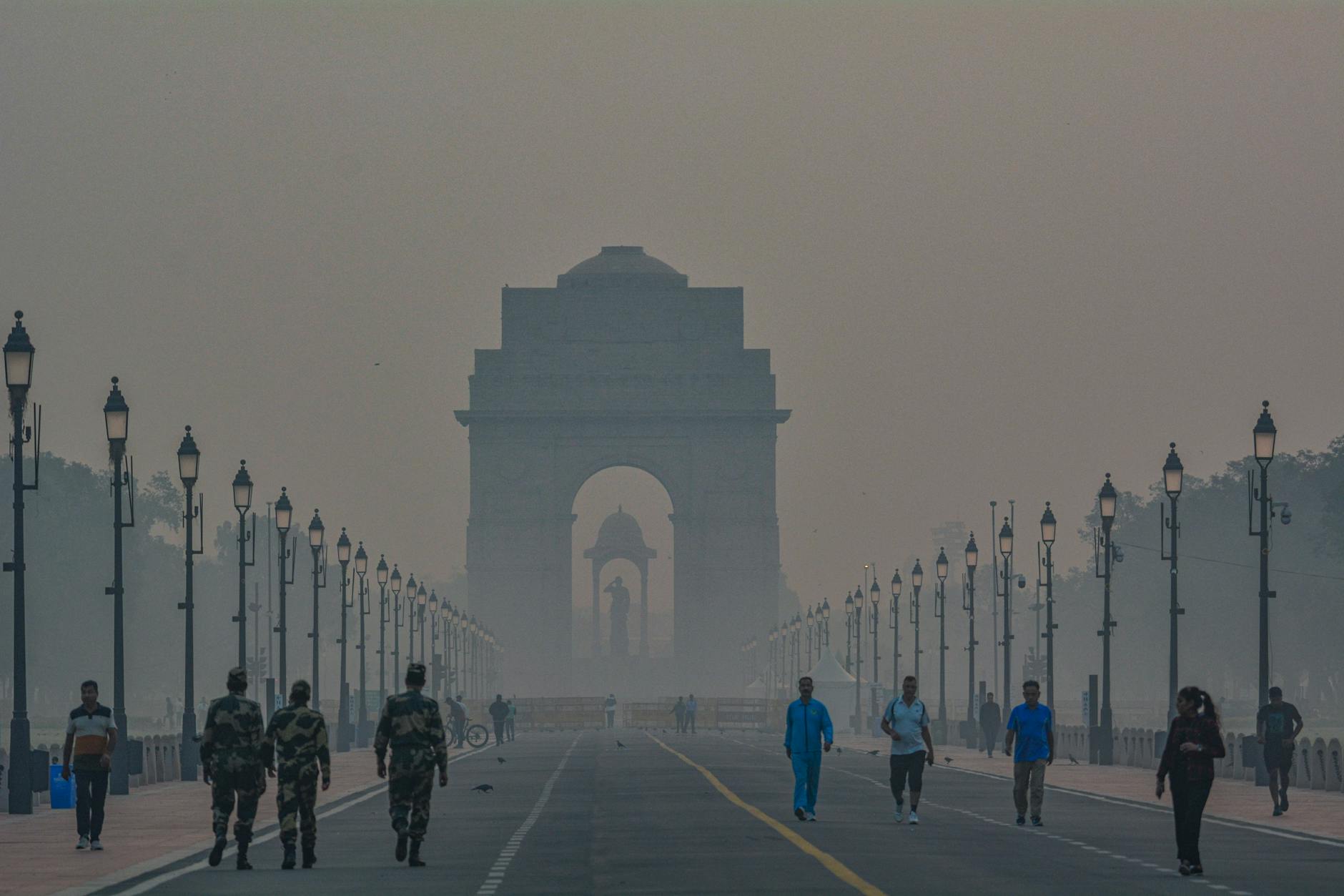 A foggy morning scene with pedestrians near India Gate in New Delhi, highlighting the landmark's grandeur.