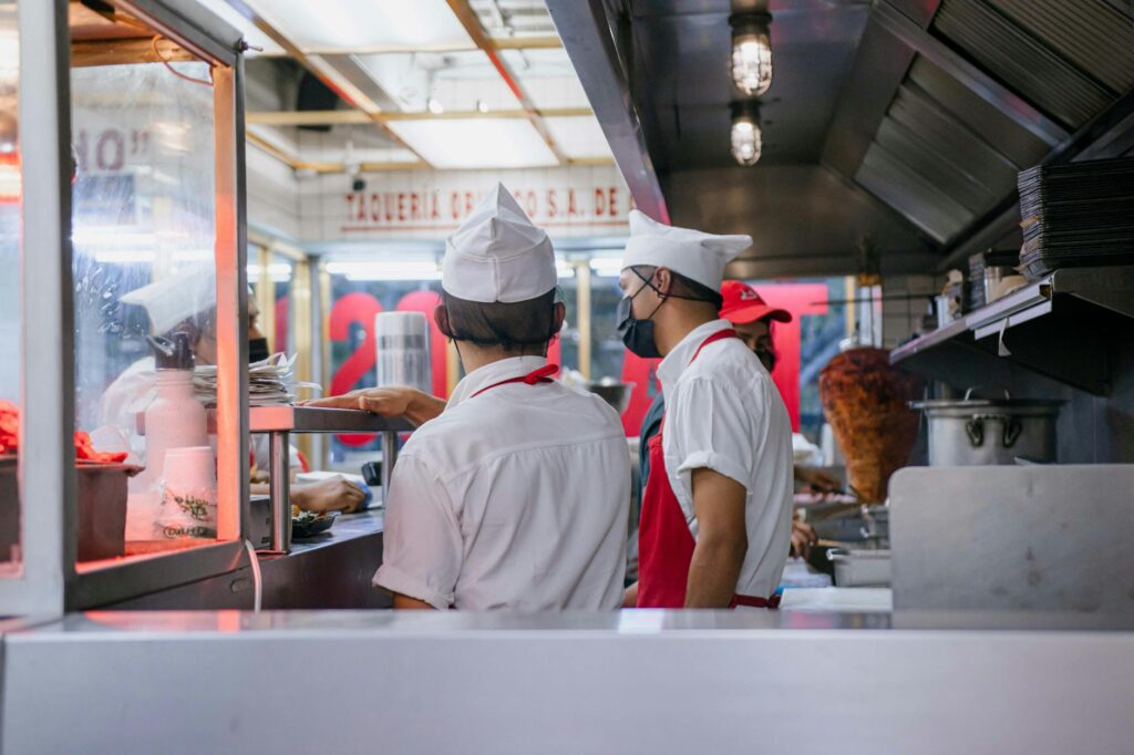 Chefs in uniforms working in an open restaurant kitchen, preparing food orders.