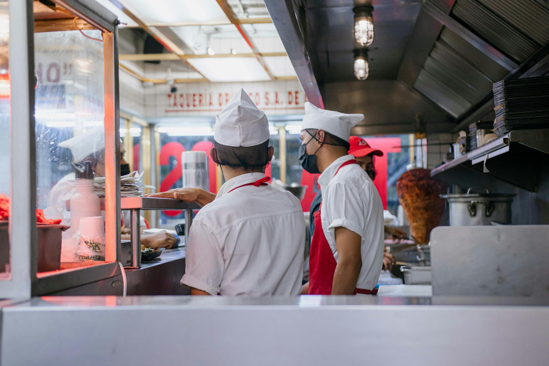 Chefs in uniforms working in an open restaurant kitchen, preparing food orders.