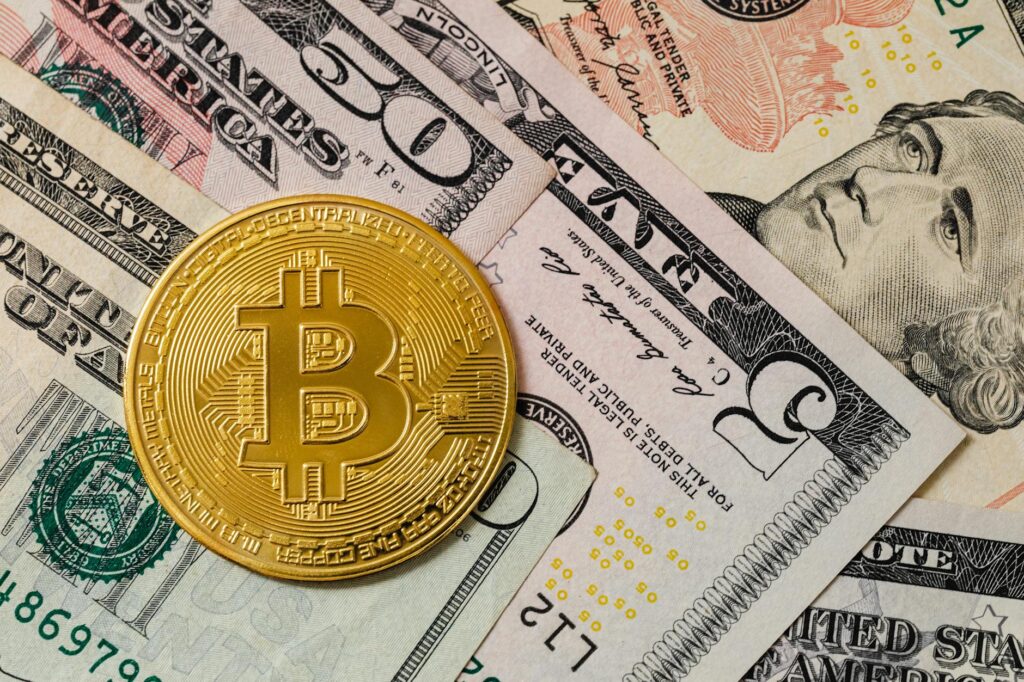 Close-up of a gold Bitcoin coin placed on various US dollar bills, illustrating digital currency concepts.