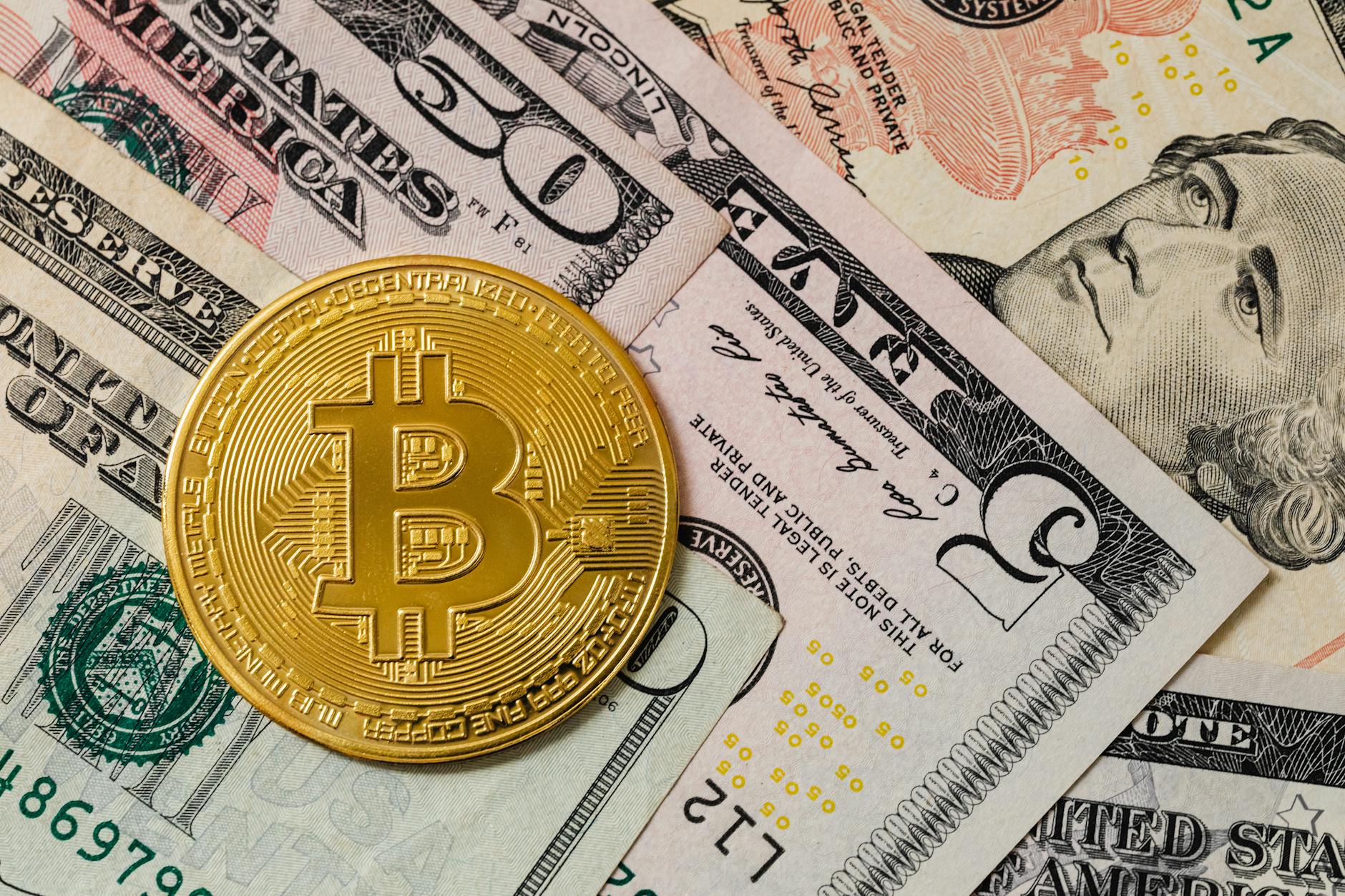 Close-up of a gold Bitcoin coin placed on various US dollar bills, illustrating digital currency concepts.