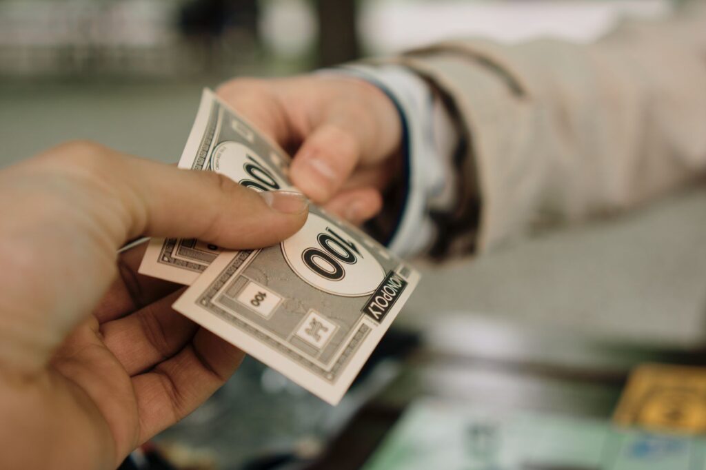 Close-up of two hands exchanging Monopoly money, symbolizing a financial transaction.